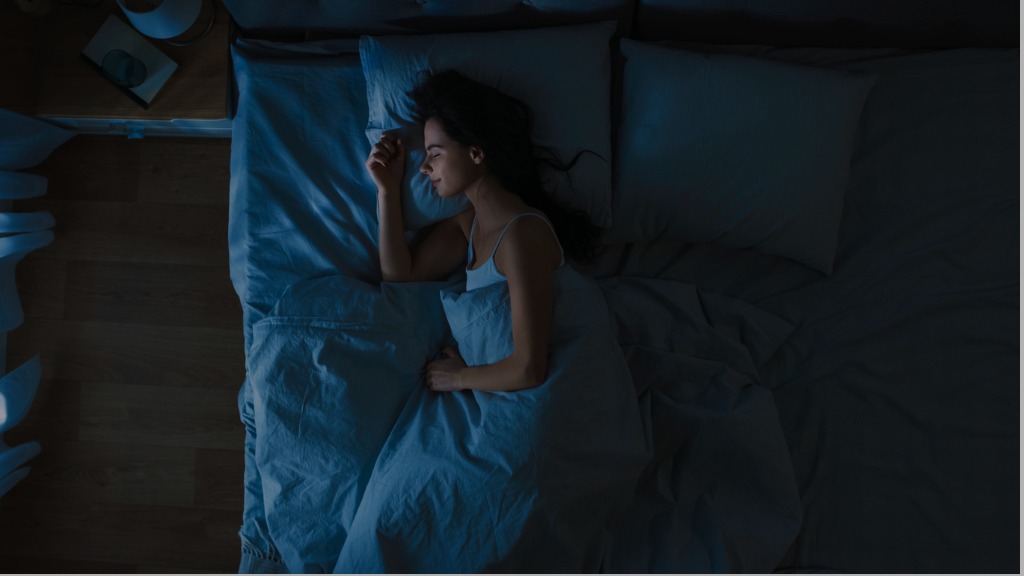 A woman sleeps soundly in a double bed with blue sheets