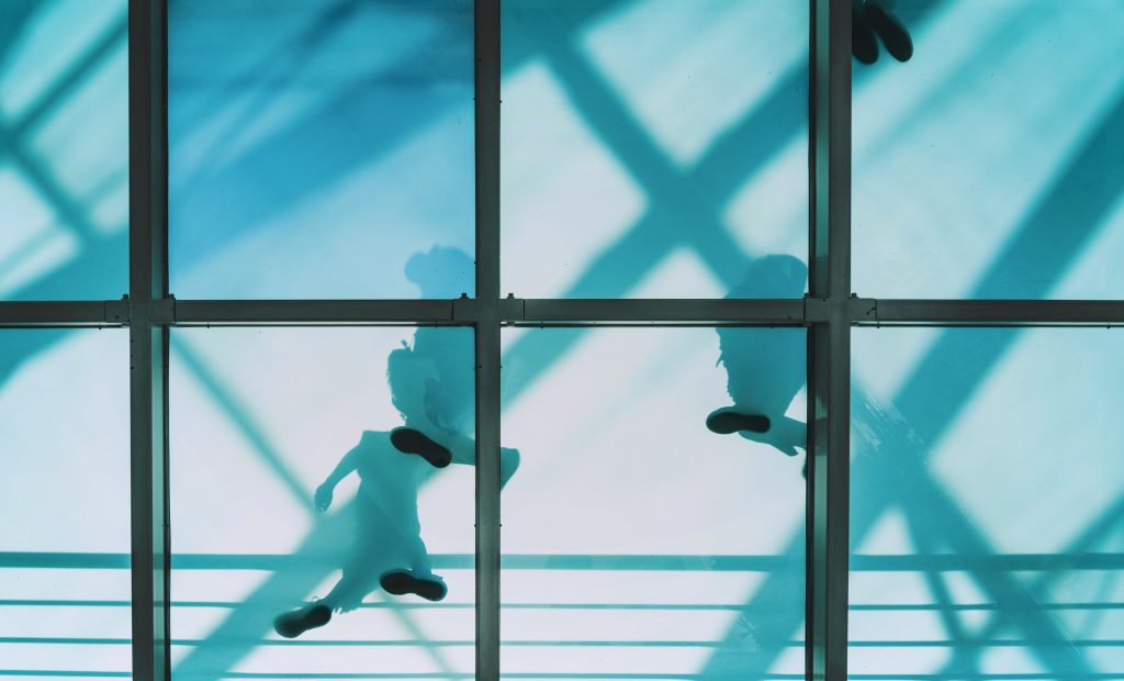 Shadow figures move above a transparent pedestrian bridge