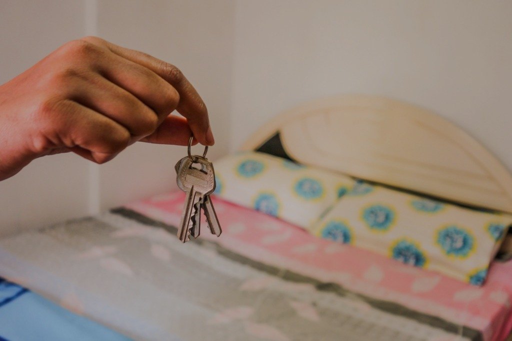 A hand holds a set of keys above a neatly made bed