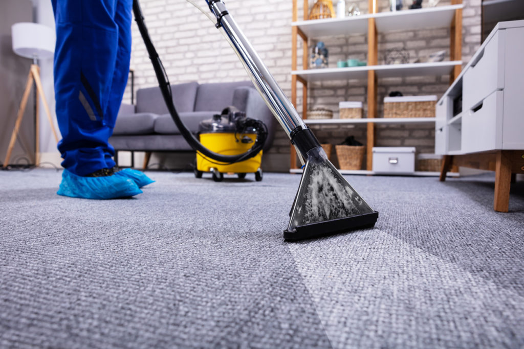 Professional cleaner hoovers carpet in a serviced apartment wearing personal protective clothing against spread of COVID-19